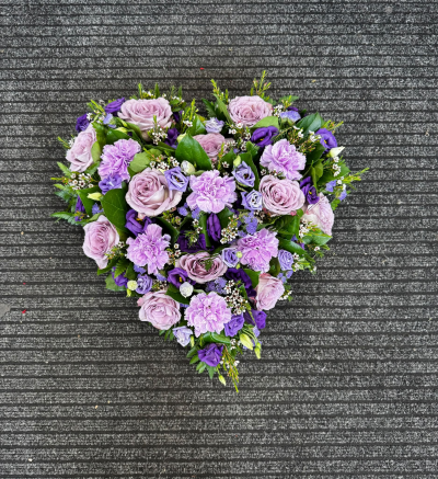 Lavender Remembrance - A beautifully arranged heart-shaped funeral tribute featuring delicate shades of lilac, lavender and rich purple, complemented by fresh greenery. This elegant design is a touching expression of everlasting love, offering a personal and meaningful way to say a final goodbye to someone dearly missed.