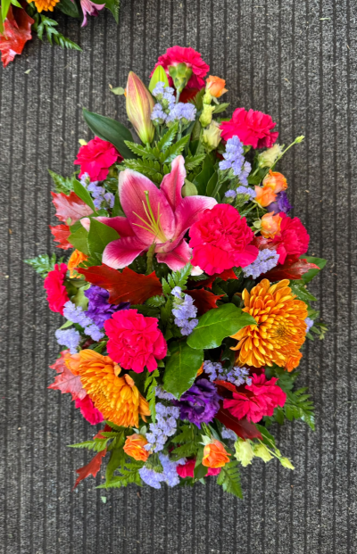 Colourful Memories - A beautiful funeral spray bursting with vibrant pink, warm orange and delicate purple tones, complemented by rich seasonal foliage. Lovingly arranged to create a striking and colourful tribute, this design is a wonderful way to celebrate a life full of love, warmth and cherished memories.