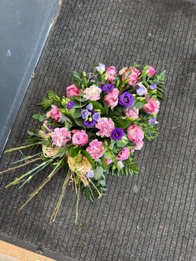 Gentle Farewell - A beautiful, natural tied funeral sheaf featuring delicate shades of pink, lilac and purple, complemented by fresh greenery. Finished with a rustic raffia bow, this elegant tribute offers a heartfelt way to express your love, sympathy and treasured memories of someone special.