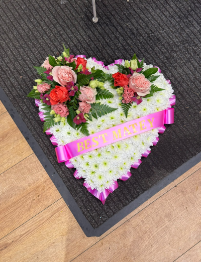 Forever in Our Hearts - A beautiful heart-shaped funeral tribute featuring a traditional white base, complemented by delicate pink, coral and purple tones. Finished with an elegant pink ribbon, this touching arrangement is a meaningful expression of everlasting love and a fitting way to say a final goodbye to someone dearly missed. Personalised ribbon lettering is available on request.